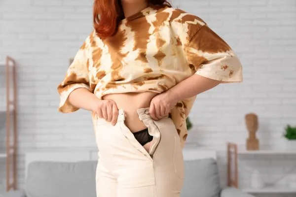 Image of woman trying to do her trousers up after pregnancy weight gain Brentford