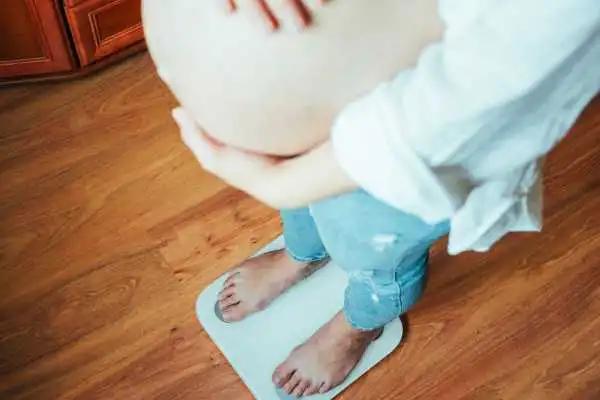 Image of woman weighing herself and experiencing weight gain through pregnancy Brentford